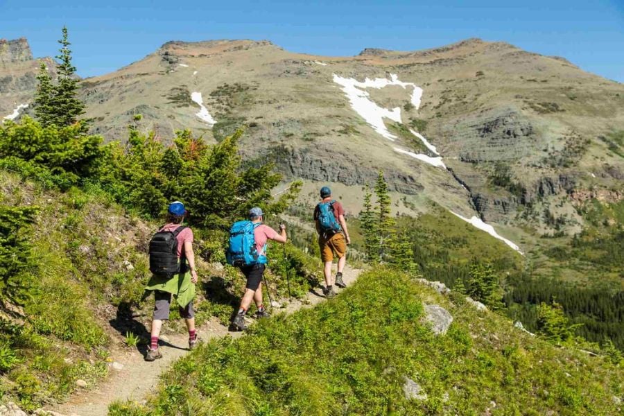 Three hikers explore a mountain trail with stunning alpine views and patches of snow.
