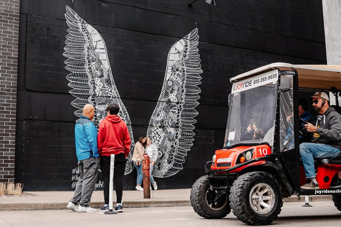 Golf cart tour in Nashville passing the famous Gulch wings mural as visitors pose for photos