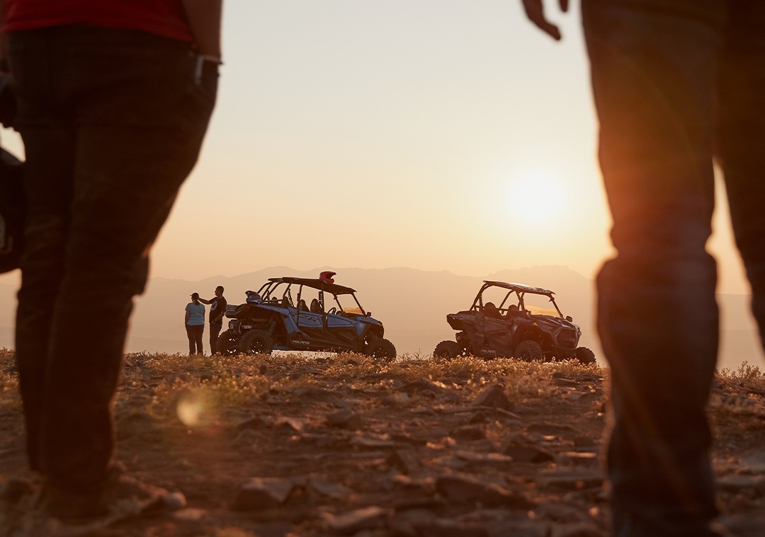 two RZR off-road vehicles and people in the sunset