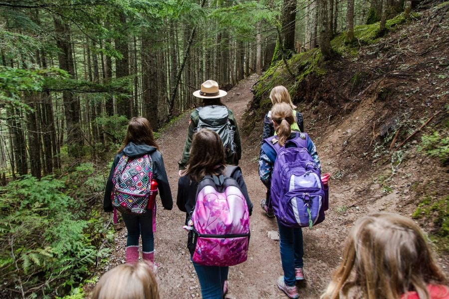 Kids follow a park ranger along a forest trail, learning about nature.
