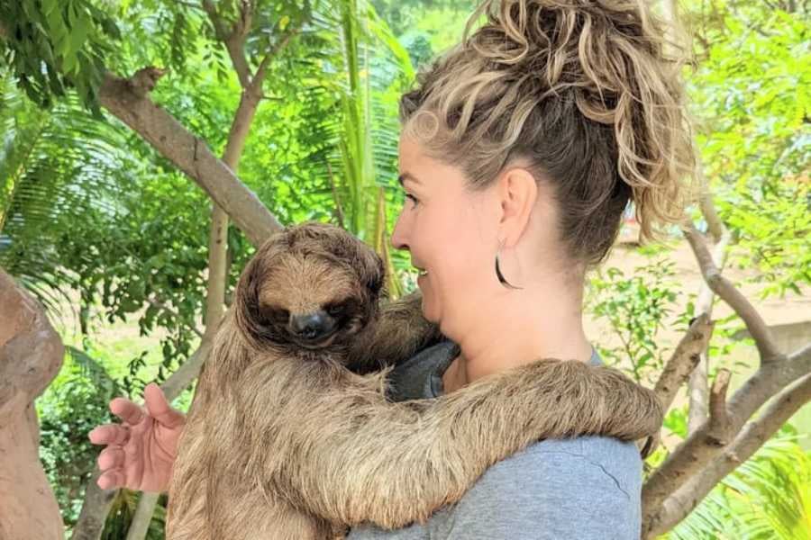 A woman smiles while holding a sloth, capturing a heartwarming moment with the slow-moving animal.