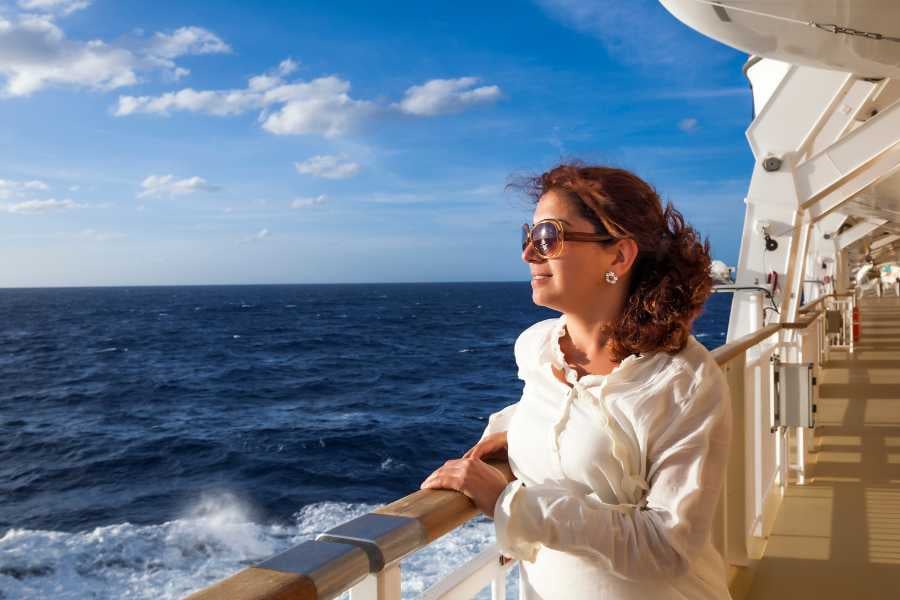 A woman on a cruise ship deck enjoying the ocean view and fresh breeze.