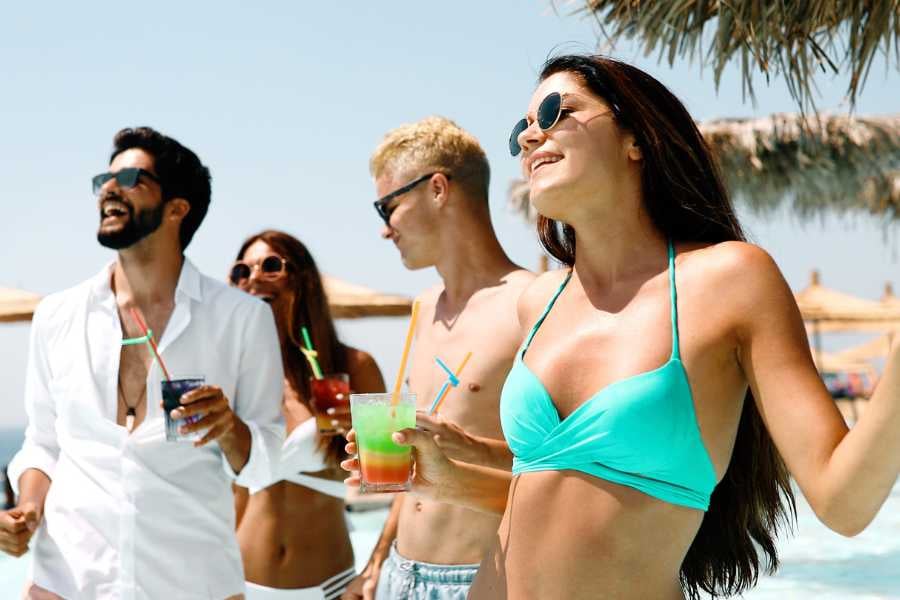 Friends laughing and sipping colorful drinks, enjoying the vibrant energy of a tropical beach day.