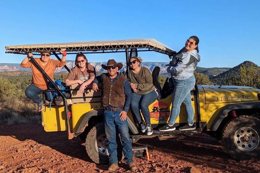 Group of friends hanging out and laughing beside their off-road tour jeep.