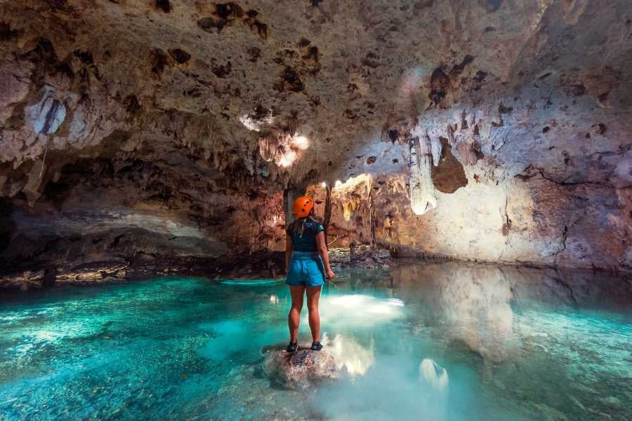 A traveler stands in awe within a glowing cave, surrounded by crystal-clear water and rugged rock formations.