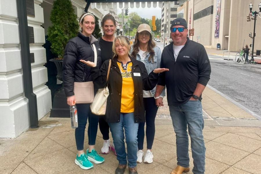 Five friends smile big outside a downtown building on a cool day.