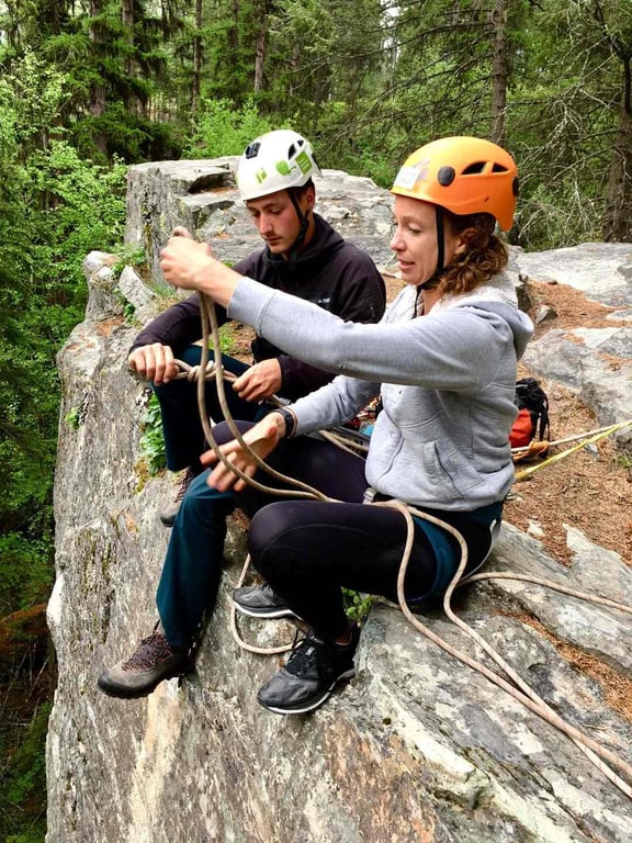 man and woman tying a knot at top of climbing route