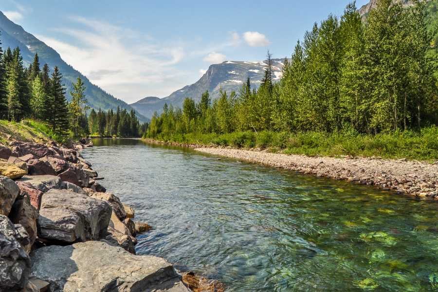 A crystal-clear river winds through a breathtaking valley with towering mountains in the distance.