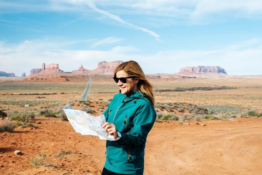 A woman reads a map while standing in a wide, open desert with mesas.